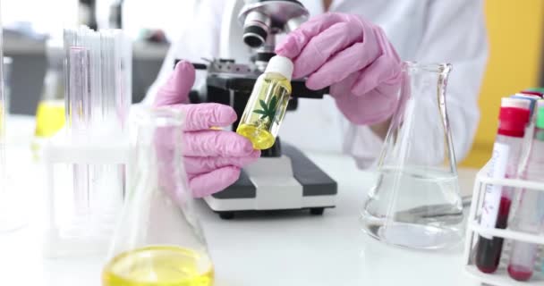 Επιστήμονας χημικός με γάντια που κρατά φιαλίδιο με λάδι μαριχουάνας μπροστά από το μικροσκόπιο σε εργαστηριακό κοντινό πλάνο 4k ταινία αργή κίνηση — Αρχείο Βίντεο