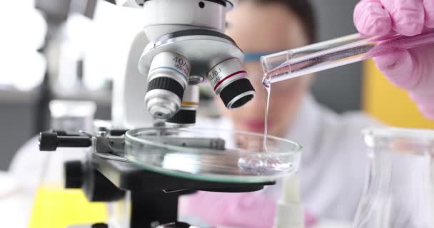 Ilmuwan kimia menuangkan deterjen ke cawan petri di depan mikroskop di laboratorium 4k film gerak lambat — Stok Video