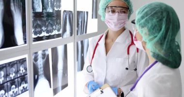 Koruyucu maskeli ve gözlüklü kadın doktorlar röntgenlere bakıyor.