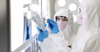 Koruyucu takım elbiseli ve maskeli iki doktor röntgenlere bakıyor.