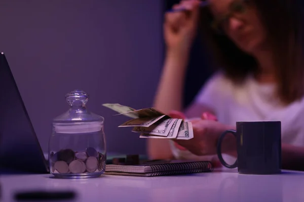 Mujer joven rota contando dinero en efectivo, contenedor de vidrio con monedas en el escritorio — Foto de Stock