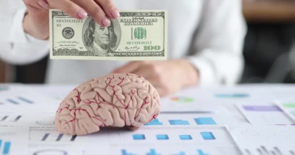 Γυναίκα χέρι εισάγοντας 100 δολάρια σε εικονική ανθρώπινο εγκέφαλο και βάζοντας κλεψύδρα στο τραπέζι closeup 4k ταινία αργή κίνηση — Αρχείο Βίντεο