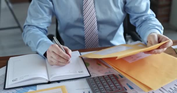 Homem classificando letras em envelopes amarelos e escrevendo em notebook close up filme 4k — Vídeo de Stock