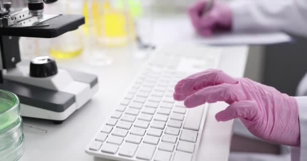 Scientist chemist with gloves typing on computer keyboard and filling out paperwork closeup 4k movie — Stockvideo