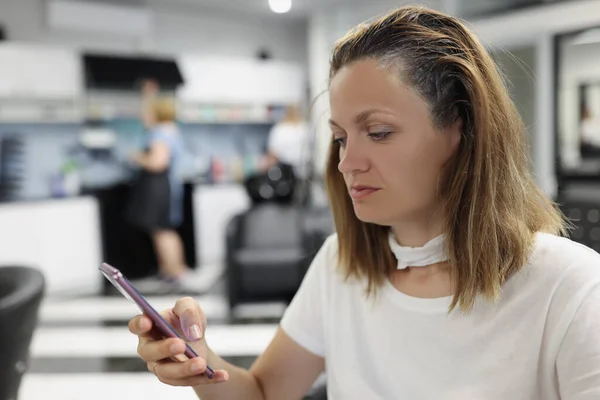 Woman client sit at hairdresser, woman use smartphone while waiting for hair to dye — Fotografia de Stock