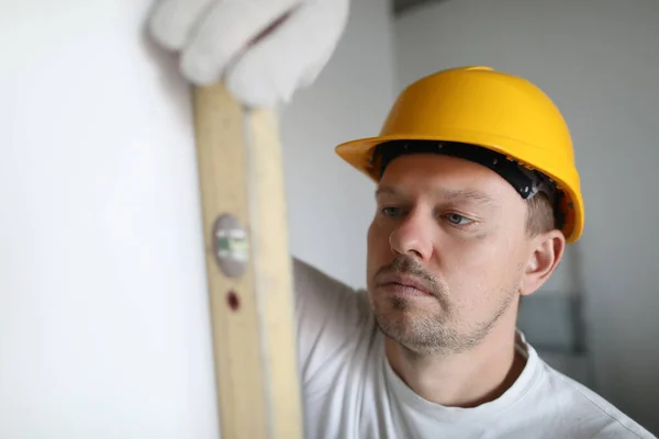 Man in helmet measuring wall using building level in apartment — Stock Photo, Image