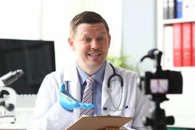 Male doctor speaking into camera in clinic clipart