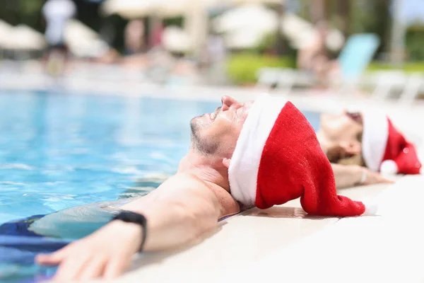 Młodzi ludzie w kapeluszach Mikołaja leżą zrelaksowani w basenie — Zdjęcie stockowe