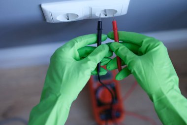 Eldivenli eller prizin yanında dijital çoklu metre tutuyor.