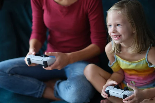 Маленька дівчинка з нянею сидить на дивані грає у відеогру — стокове фото