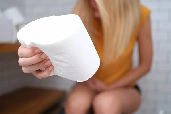 Une femme est assise sur les toilettes avec du papier toilette à la main — Photo