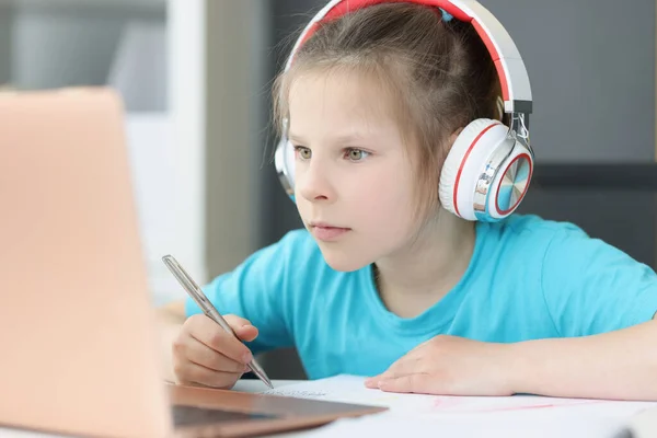Uma menina em fones de ouvido olha atentamente em um laptop — Fotografia de Stock