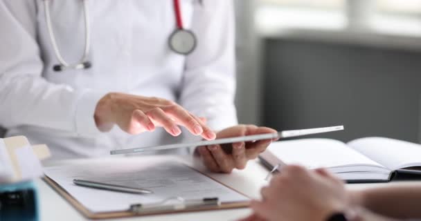 El médico trabaja con el paciente en la clínica, estudiando el diagnóstico en la tableta — Vídeo de stock