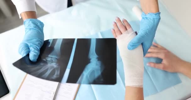 El médico sostiene la radiografía de la mano y examina el brazo dolorido del paciente — Vídeo de stock