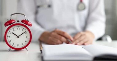 Red alarm clock standing on table in front of doctor closeup 4k movie slow motion