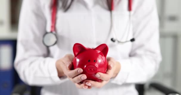 Doctor holding red piggy bank in clinic closeup 4k movie slow motion — Vídeos de Stock