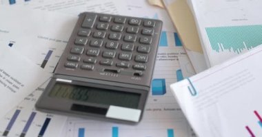 Calculator lying on documents with graphs in office 4k movie slow motion