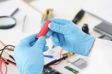 Male in blue gloves holding red battery piece, repairing broken or damaged device by himself