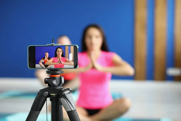 Camera on tripod filming people perform asana on mat in studio — Fotografia de Stock