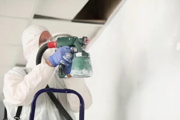 Male worker painting wall with spray gun in white colour, busy handyman at work — Stok Foto