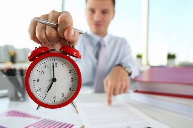 Man hand on red alarm clock stands at desk in office showing seven oclock AM PM