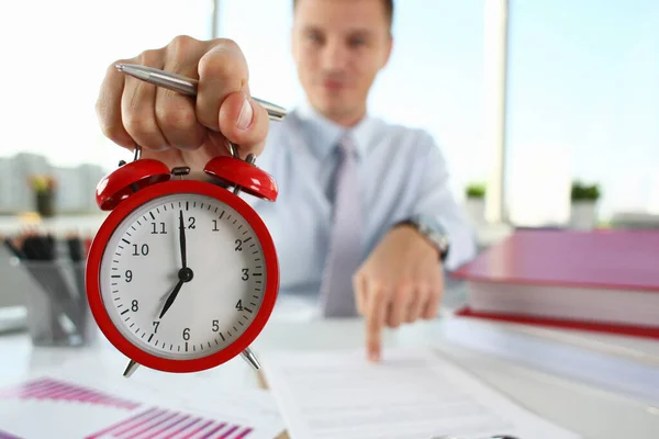 Man hand on red alarm clock stands at desk in office showing seven oclock AM PM — Zdjęcie stockowe