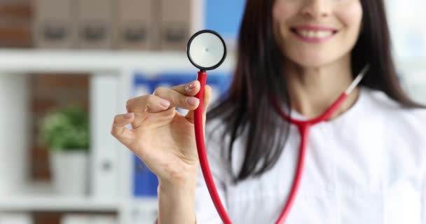 Una doctora sonriente con bata blanca sostiene estetoscopio — Vídeo de stock