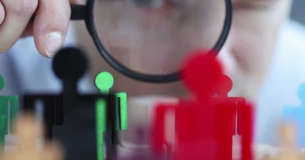 Businessman looks through magnifying glass at figures of people — Αρχείο Βίντεο