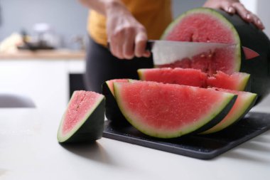 Woman at home kitchen cuts watermelon, hands close-up