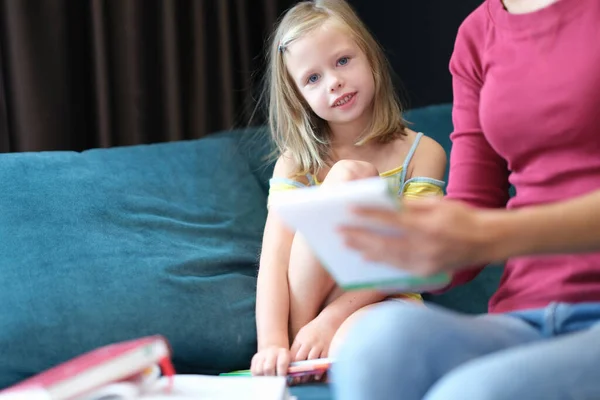 A little girl with her mother are sitting on the couch with books — Stockfoto