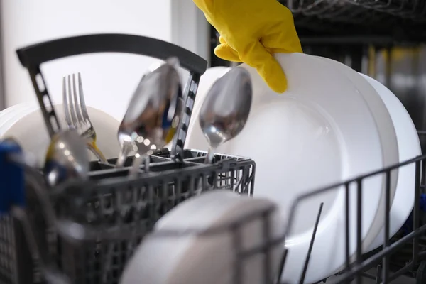 A hand in a yellow glove pulls dishes out of the dishwasher — Fotografia de Stock