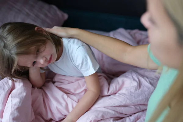 Mom strokes a frustrated little girl on the bed at home — Foto Stock