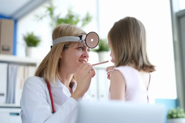 Woman pediatrician looks at the throat of a little girl — Photo