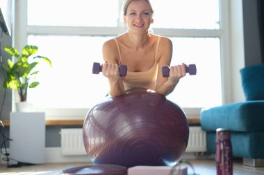 Woman doing exercises with dumbbells on a burgundy ball