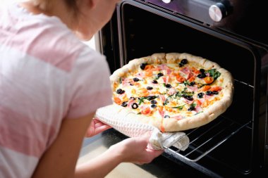 A woman takes out a hot homemade pizza from the oven