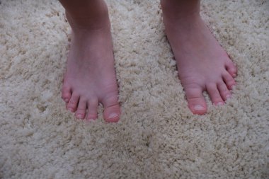 Bare feet of an adult on a soft beige carpet, close-up