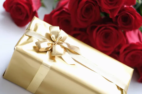 Big golden gift box on the background of red roses — Stockfoto