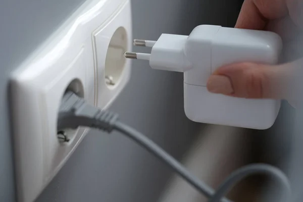 Female fingers plug the power adapter into an outlet — 图库照片