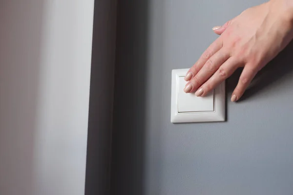 A beautiful female hand presses the switch on the wall — Stockfoto