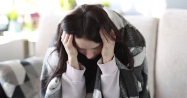 Kafasında baş ağrısı ve şakakları olan bir kadın kanepede oturuyor.