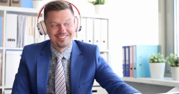 Młody mężczyzna w słuchawkach klika i tańczy w miejscu pracy — Wideo stockowe