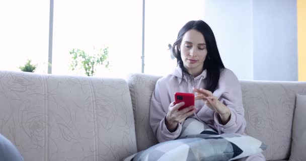 Mujer joven y relajada usando el teléfono inteligente está navegando en las redes sociales y revisando noticias — Vídeos de Stock