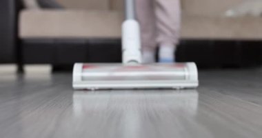 Kadın modern oturma odasında kablosuz elektrik süpürgesiyle yerleri süpürüyor.