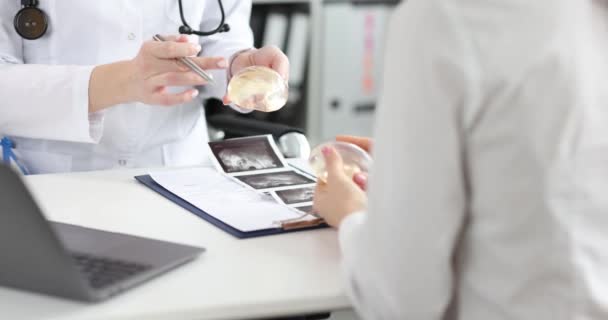 Médico cirurgião mostra implante mamário de silicone para paciente na clínica — Vídeo de Stock