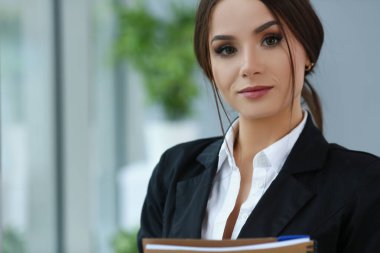 Güzel gülümseyen tezgahtar takım elbise giyer iş yerinde defteri tutar, kameraya bakar.