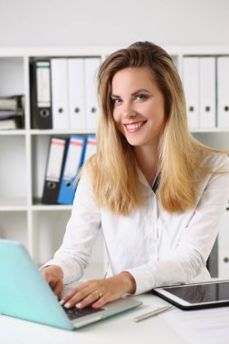 Neşeli genç ofis çalışanı çalışma yerinde oturup internetten bilgi topluyor.