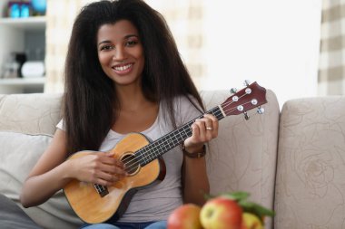 Mutlu Afro-Amerikan kadın evde, oturma odasında ukulele çalıyor.