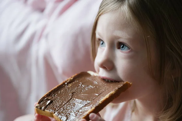 Little cute girl eating bread with chocolate pasta on top, tasty sweets