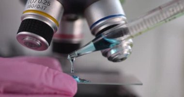 Bilim adamı kimyager, laboratuvarda mikroskobun önüne mavi sıvıyı döküyor.