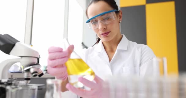 Donna farmacista guardando fiaschetta con liquido giallo davanti al microscopio in laboratorio 4k film slow motion — Video Stock